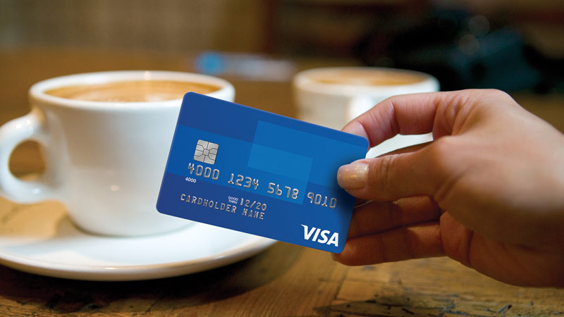 Woman’s hand holding credit card with two coffee’s on the table.